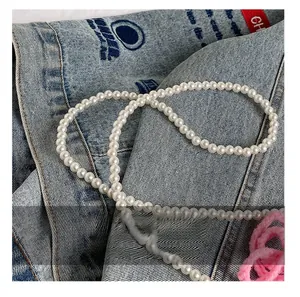Detail shot of lustrous white pearl strap on denim fabric for cross body handbag