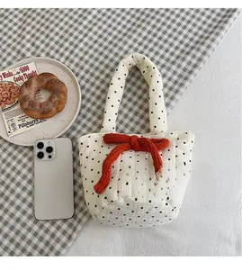 Detailed view of white quilted cotton handbag with large orange knitted bow accent