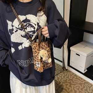 Retro leopard print crossbody bag with brown leather handles and plush charm accessory