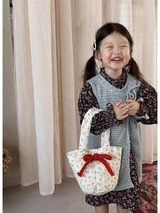 Detail of a quilted cream tote bag featuring a decorative red knitted bow accessory