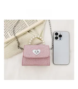 Mini sac tissé rose avec poignée en perles et fermoir cœur argenté à côté d'un smartphone
