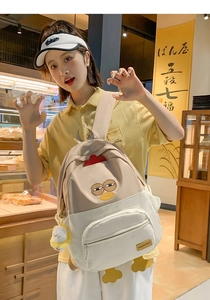Close-up of cute chick-themed backpack with 3D comb and plush keychain in cafe setting
