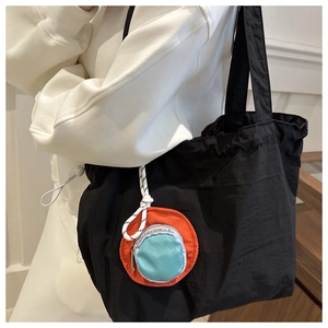 Detail einer leichten schwarzen Nylon-Einkaufstasche mit orange-blauer kleiner Geldbörse