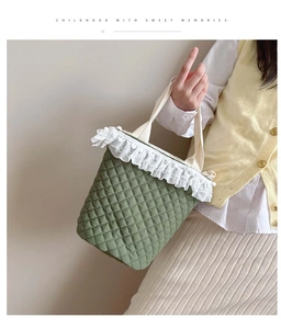 Detail der grünen Stepptasche mit weißem Spitzenbesatz und flauschigen Pompons am Griff