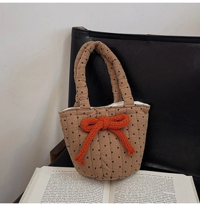 Brown canvas polka dot tote bag with a large orange woven bow on a leather chair
