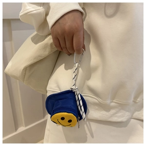 Detail der blauen Mini-Hut-Geldbörse mit gelbem Smiley-Stickerei auf einem cremefarbenen Pullover