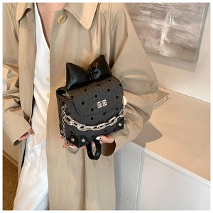 Close-up of a gray polka dot bag featuring a large black bow and silver chain strap