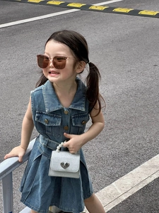 Fille en robe denim sans manches bleu foncé avec sac à main cœur et poignée perle