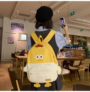 Detail view of a cute yellow chick cartoon backpack on a model in a cafe setting
