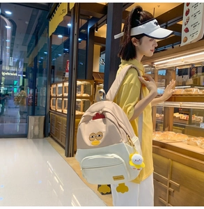 Detail of cute cartoon chick backpack featuring plush pendant and embroidery on beige fabric