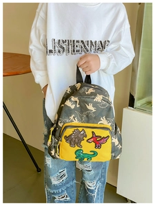 Dettaglio ricami dinosauro su zaino mimetico grigio per bambini con tasca gialla