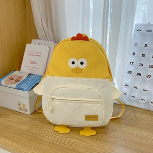 Detail of cute yellow chicken backpack with red comb and creative beak design on a wooden table