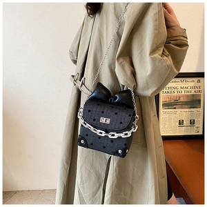 Chic polka dot crossbody bag with a large bow and silver chain on a trench coat
