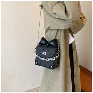 Close-up of black polka dot crossbody bag with leather bow on model's shoulder