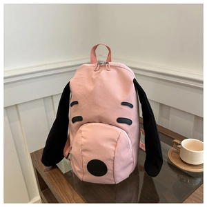 Detailed view of a pink canvas puppy backpack featuring long black ears on a wooden table