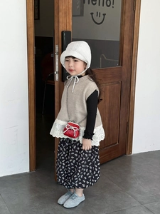 Dettaglio di una bambina con gilet in maglia beige e mini borsa rossa con catena
