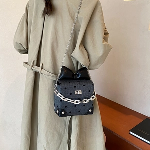 Polka dot crossbody bag with large bow and silver chain strap shown on a beige trench coat