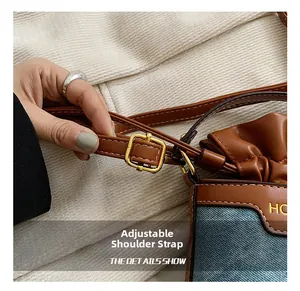 Detail showing adjustable strap with gold buckle on brown leather and denim crossbody bag