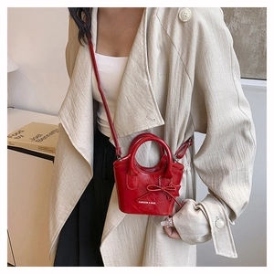 Close-up of a red patent leather mini handbag with a bow detail on a model in beige coat