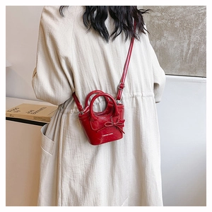 Back view of a stylish red mini bucket crossbody bag with a bow charm on a beige coat