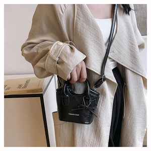 Detail of a mini black bucket bag featuring star charm and bow tie on leather texture