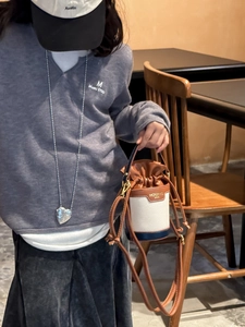 Close-up of tricolor leather bucket bag with chain strap and heart necklace on child model
