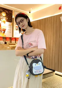 Detail of cute cartoon penguin crossbody bag with blue bow and plush charm on a model