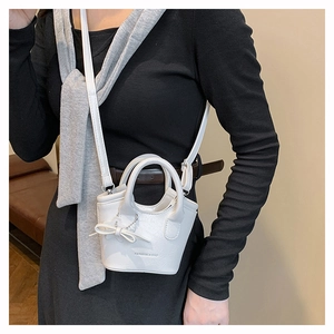 Close-up of a white mini bucket bag with ribbon charm and crossbody strap for women