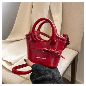 Detail of red mini bucket bag featuring a bow, metallic chain, and glossy embossed texture