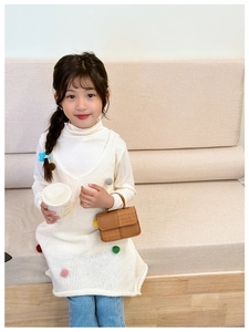 Détail de la robe tricotée blanche pour filles avec pompons colorés et sac à main marron texturé