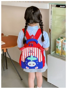 Detail of red and blue strawberry backpack worn by a child in a cozy indoor setting