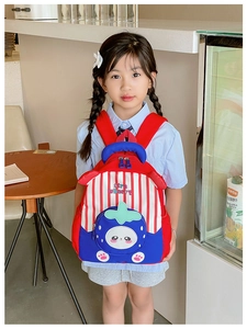 Asian girl wearing a red and blue strawberry striped backpack in a cozy indoor setting