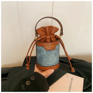 Detail of mini denim bucket bag featuring brown leather trim and drawstring closure