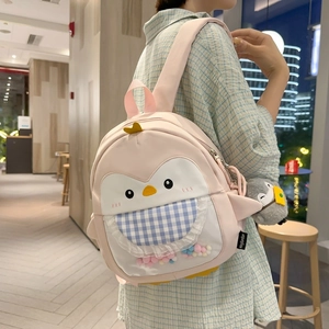 Detail of pink cartoon penguin backpack with colorful pom-poms and cute plush charm
