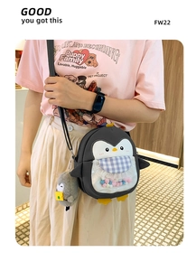 Detail view of cartoon penguin crossbody bag with colorful pom-poms and plush charm
