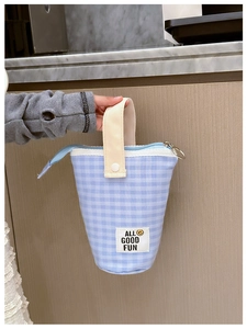 Détail d'une trousse à carreaux vichy bleus avec écusson sourire et anse crème pratique
