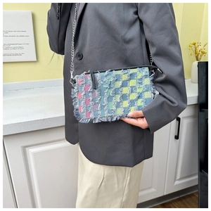 Detail of colorful plaid denim crossbody bag with frayed edges and silver chain strap