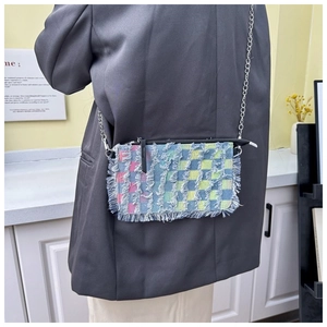 Detail of colorful plaid denim crossbody bag with fringe trim and silver chain on model