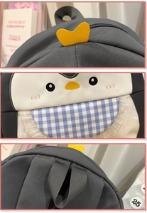 Detail showing cartoon penguin embroidery and blue checkered pattern on dark grey nylon bag