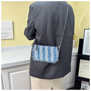 Denim crossbody bag with frayed striped patterns worn over a grey blazer and skirt