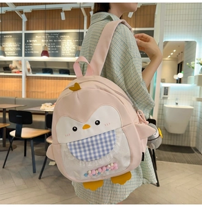 Pink penguin backpack with transparent window and colorful pom-poms shown on model