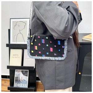 Detail of denim crossbody bag with colorful patches, fringe trim and silver chain strap