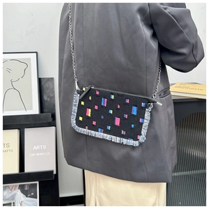 Detail of crossbody bag with colorful square patterns and denim fringe accents on black fabric