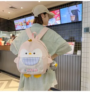 Pink penguin backpack with cartoon face, plush charm and colorful pom-poms in clear pocket