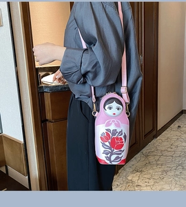 Detail of pink Matryoshka doll crossbody bag with floral patterns on a side-wearing model