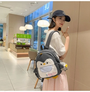 Detail of dark grey penguin backpack with transparent pocket and colorful plush ball charms