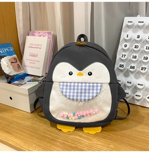 Detail of cute penguin backpack featuring a transparent pocket filled with colorful pom-poms