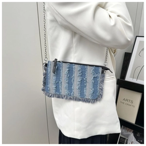 Detail of denim patchwork crossbody bag with frayed edges and silver chain strap