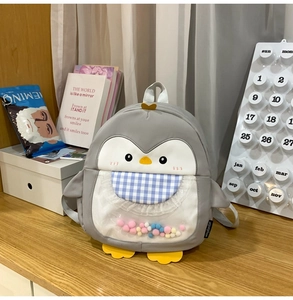 Detail of penguin backpack featuring clear front pocket with colorful pom-poms inside
