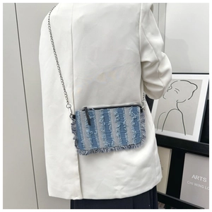 Detailed back view of a light blue denim crossbody bag with fringe on a white blazer